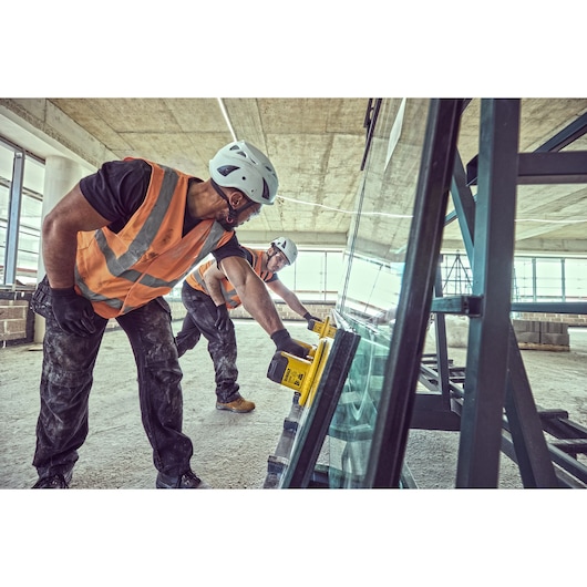 Two construction workers prepare to lift a large pane of glass using Grabo 18V XR Suction Lifters