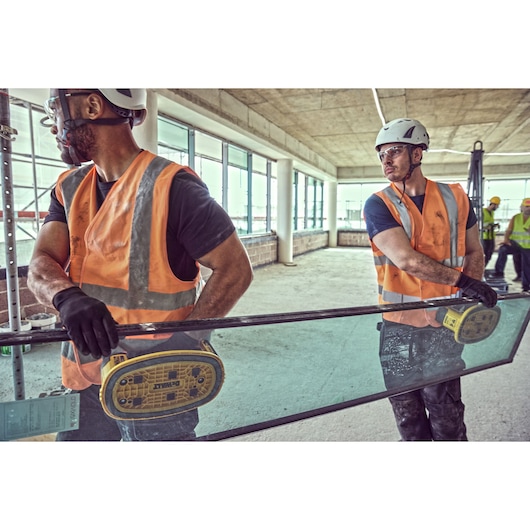 Two construction workers use Grabo 18V XR Suction Lifters to transport a large pane of glass