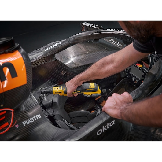 Mechanic using the DEWALT 18V XR Brushless ¼” Ratchet with 18V POWERSTACK battery to tighten bolts in the seat frame cockpit of the F1 McLaren racing car