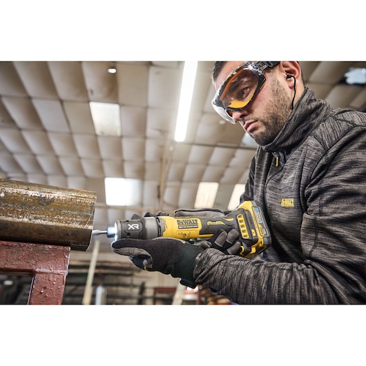Worker uses the DEWALT 18V XR Compact Inline Grinder to smooth a metal surface