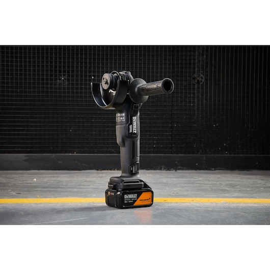 DEWALT x McLaren F1 Team 18V XR Special Edition Grinder with 5Ah battery standing vertically on a concrete floor