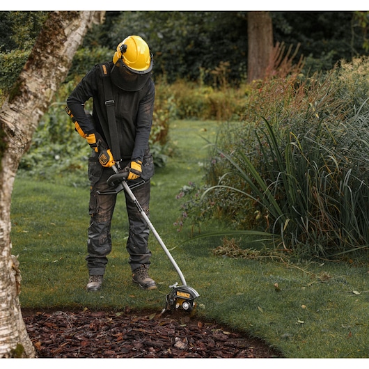 Worker using  a DEWALT split boom with the DEWALT DCMASED9N Edger Attachment to trim grass edging