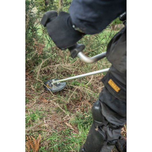 Close up of landscaper using the DEWALT 54V Brush Saw (Bull Handle) to cut branches.