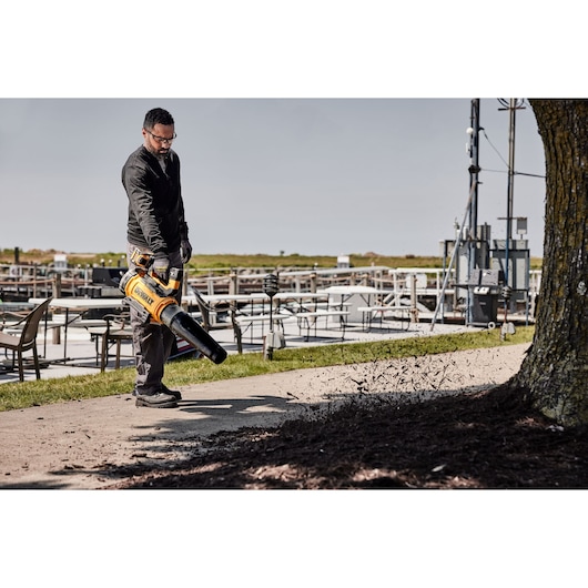 Worker using 54V Axial Blower DCMBL777 to clear bark away from a pavement