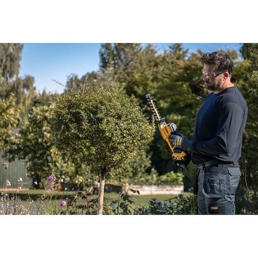 Worker using the DEWALT 18V XR Compact Hedge Trimmer to trim a small tree
