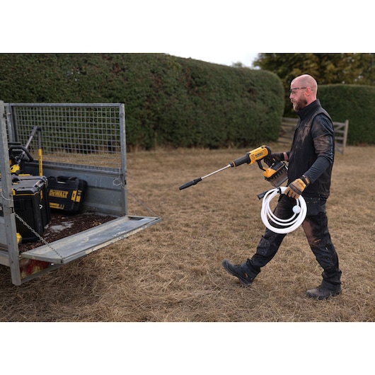 Man walking towards an open trailer holding the DEWALT 54V XR FLEXVOLT Power Cleaner with hose