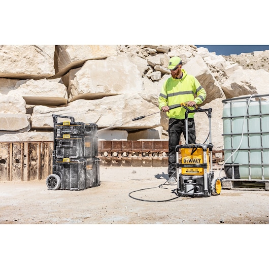 Worker cleaning a stack of Toughsystem boxes with the Dewalt 2 x 18V Cordless Pressure Washer