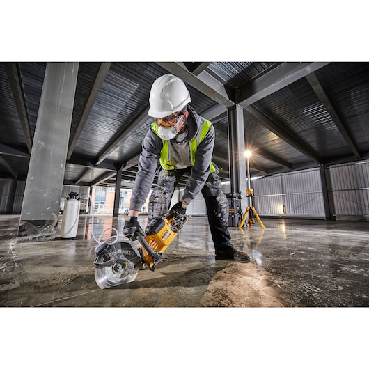 Profile of brushless cordless cut-off saw being used by person on concrete vertically.