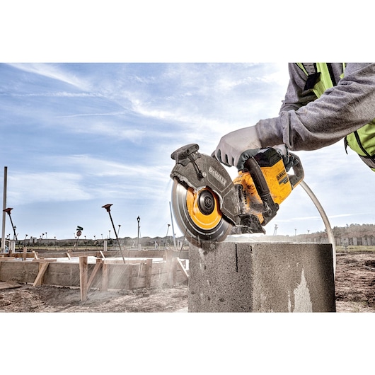 Brushless cordless cut-off saw cutting concrete block outdoors.