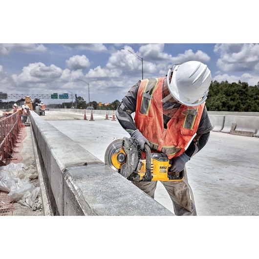 Brushless cordless cut-off saw being used by person on concrete by roadside.
