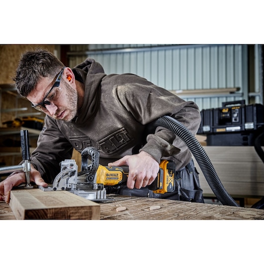 A PERSON USING A DCW682 18V XR BISCUIT JOINTER WITH A 5AH BATTERY ON OAK TIMBER IN A WORKSHOP A PERSON USING A DCW682 18V XR BISCUIT JOINTER WITH A 5AH BATTERY ON OAK TIMBER IN A WORKSHOP