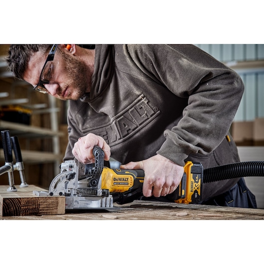 A PERSON USING A DCW682 18V XR BISCUIT JOINTER WITH A 5AH BATTERY ON OAK TIMBER IN A WORKSHOP A PERSON USING A DCW682 18V XR BISCUIT JOINTER WITH A 5AH BATTERY ON OAK TIMBER IN A WORKSHOP