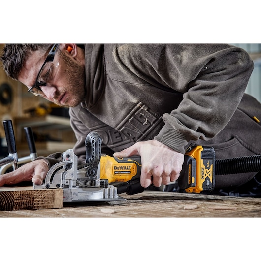 A PERSON USING A DCW682 18V XR BISCUIT JOINTER WITH A 5AH BATTERY ON OAK TIMBER IN A WORKSHOP