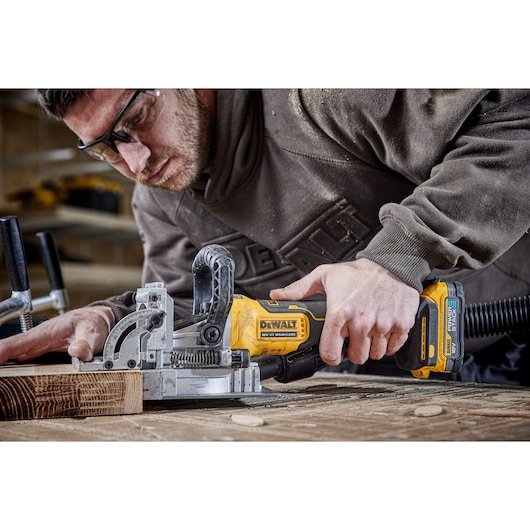 A PERSON USING A DCW682 18V XR BISCUIT JOINTER WITH A 5AH BATTERY ON OAK TIMBER IN A WORKSHOP