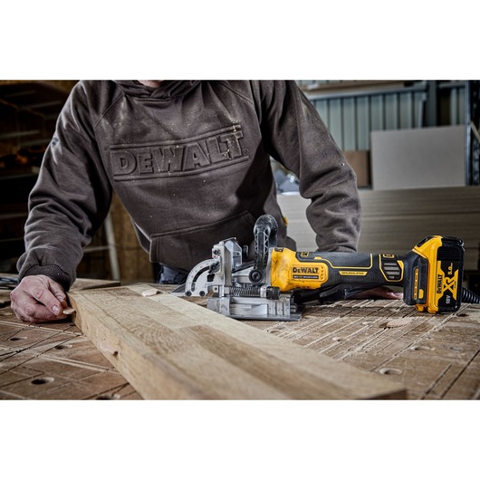 A PERSON INSERTING A WOODEN BISCUIT INTO A PIECE OF OAK TIMBER THAT HAS BEEN CUT WITH THE DCW682 18V XR BISCUIT JOINTER