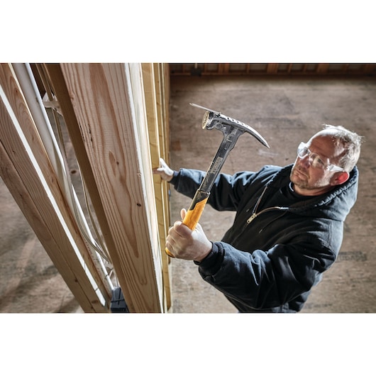 Mig weld checkered framing nailing hammer being used to hammer mounted nail into a wooden wall by a person.