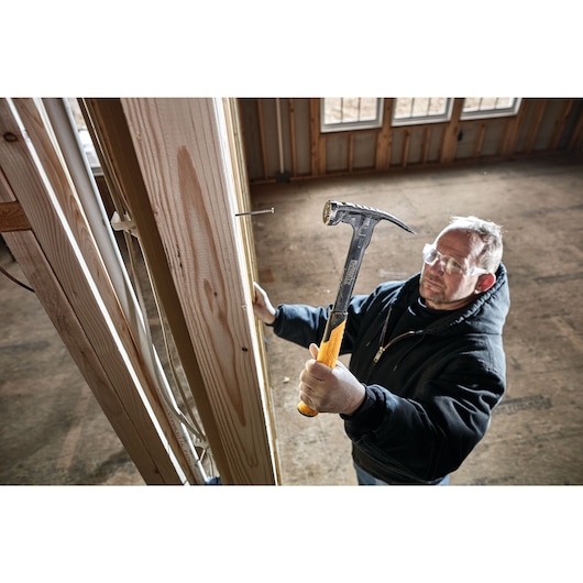 Mig weld checkered framing nailing hammer being used to hammer a nail into a wooden wall by a person.