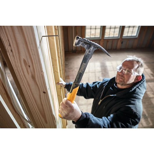 Mig weld checkered framing nailing hammer being used to hammer a nail into a wooden wall by a person.