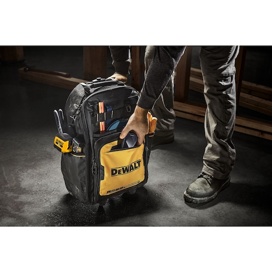 Person adding an accessory into the front pocket of the Dewalt Pro Backpack on Wheels, on a construction site