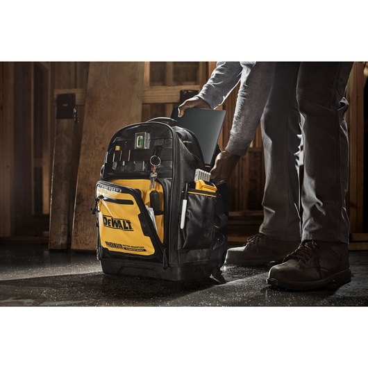 Person adding a laptop into the Dewalt Pro backpack, on a construction site Person adding a laptop into the Dewalt Pro backpack, on a construction site